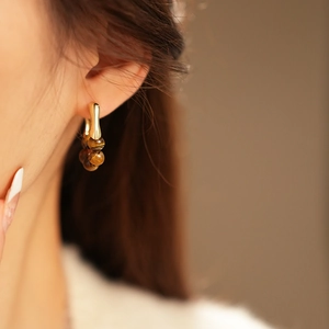 Detail of gold-plated hoop earrings with tiger eye beads worn by a female model