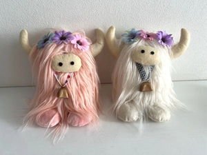 Close-up of pink and white Highland cow plush toys with flower crowns and bells