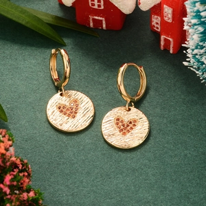 Gros plan de boucles d'oreilles huggie dorées avec charms cœur sur fond festif