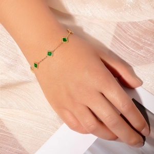 Close-up of gold chain bracelet with square green zircons on a soft silk fabric