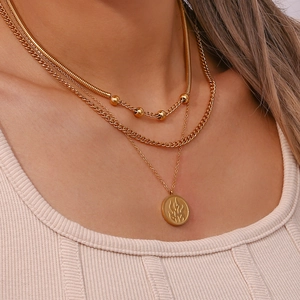 Close-up of three-layer gold necklace featuring snake chain beads and flame pendant