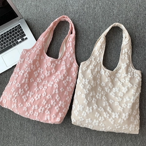 Close-up of pink and beige floral textured knit tote bags on a gray carpet background