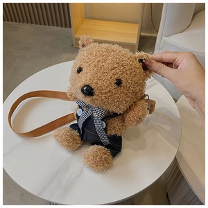 Close-up of a brown plush teddy bear bag wearing denim overalls and a checkered bowtie