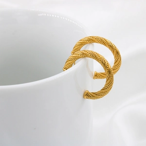 Minimalistische C-förmige gedrehte Goldohrringe am Rand einer weißen Keramiktasse