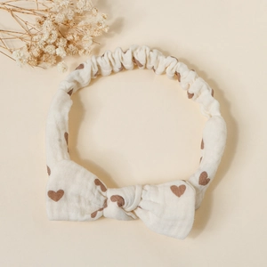 Detailed texture of baby cotton bow headband with brown heart prints on cream fabric
