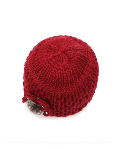 Top-down view of a dark red knitted hat with faux fur pom-poms and subtle silver sequins