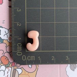 Macro shot of a small 2cm pink resin J-shaped accessory on a black metric cutting mat