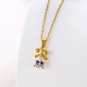 Detail of gold bow necklace with pear-shaped zircon pendant on a textured white background