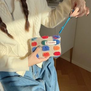 Detail of beige plush bucket bag with colorful pom-poms and blue woven handle
