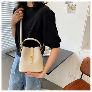 Detail of a chic cream-white bucket bag with gold clasp held by a model in a cozy cafe