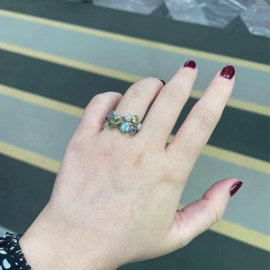 Detail of silver clustered ring with blue and green gems worn on model finger
