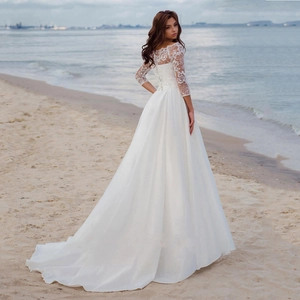 Elegant white A-line lace wedding dress with long sleeves and open back on a beach