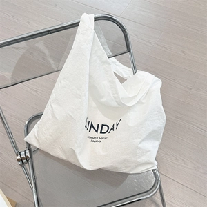 Detail of white canvas tote bag with black letter print hanging on a chair