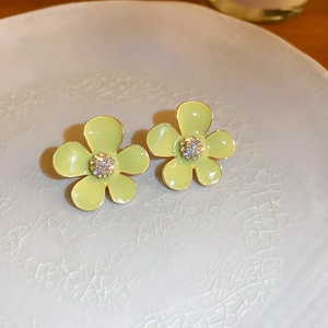 Detail of yellow enamel flower earrings with white crystals on a white ceramic plate