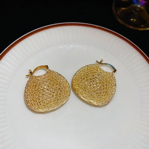 Detailed view of golden oval hollow woven earrings on a textured white porcelain plate