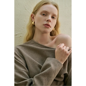 Detail view of gold geometric metal earrings paired with a brown ribbed knit top