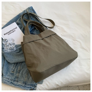 Flat lay of army green nylon shoulder bag with strap and denim jacket on white bedsheet