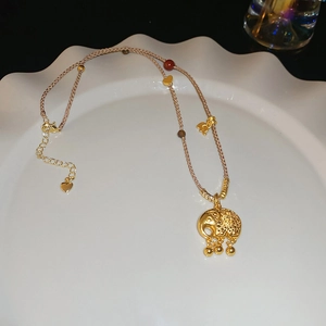 Dettaglio macro del ciondolo a forma di elefante dorato su collana in corda beige intrecciata