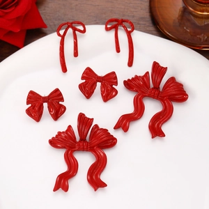 Three pairs of elegant red bow earrings in various styles on a white ceramic plate
