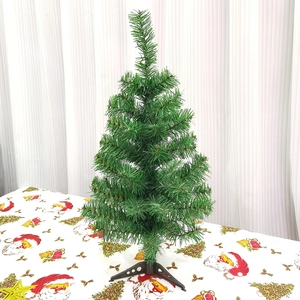 Mini artificial green Christmas tree with black stand on festive tablecloth