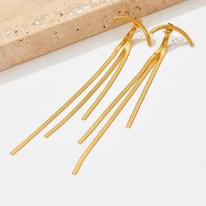 Polished gold snake chain tassel drop earrings shown on a minimalist stone display base
