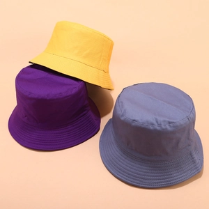 Three solid color cotton bucket hats in yellow, purple and grey blue on orange background