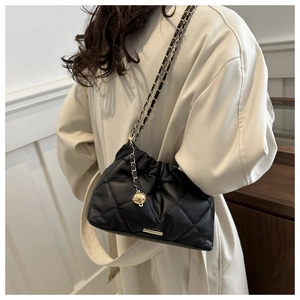 Detail view of black quilted bucket bag with gold chain strap and spherical pendant