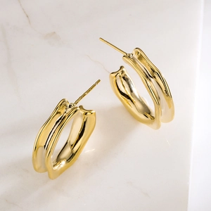 Irregular C-shaped gold-plated metal earrings on a marble surface with wave design