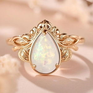 Macro detail of leaf-patterned golden ring with a pear-shaped white opal stone
