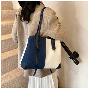 Detail of contrast color denim tote bag with leather straps on model's shoulder