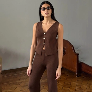 Dettaglio di un gilet in maglia marrone con scollo a V, bottoni dorati e pantaloni