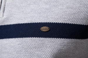 Detailaufnahme von grauem Strickstoff mit blauen Streifen und Markenlogo-Plakette