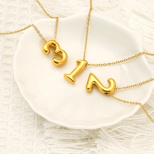 Collier avec pendentif chiffre doré en acier titane sur une élégante assiette coquillage