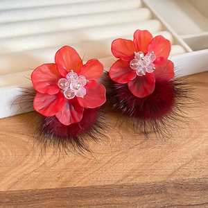Macro shot of red acrylic flower earrings with plush fur balls and crystal details