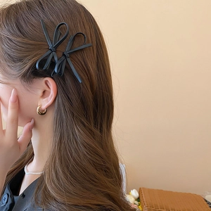 Close-up of a pair of black faux leather bow hair clips on a model with side profile