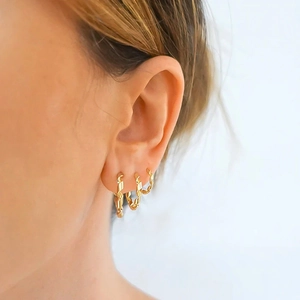 Close-up of three layered gold twisted rope hoop earrings of different sizes on a model