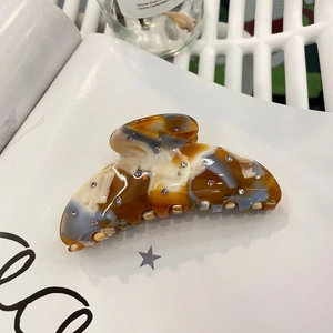 Tortoiseshell acetate hair claw clip with colorful rhinestones on a white magazine background