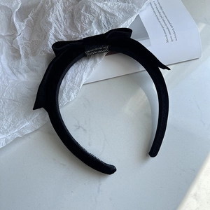 Elegant black velvet bow headband with high crown design on white marble surface