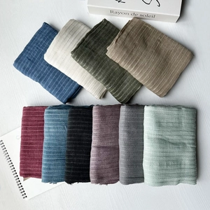 Multiple colors of striped modal silk scarves neatly folded on a white wooden table