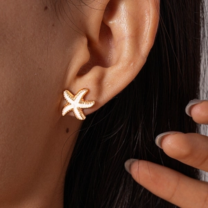 Detail shot of golden starfish stud earring with white inlay worn on earlobe