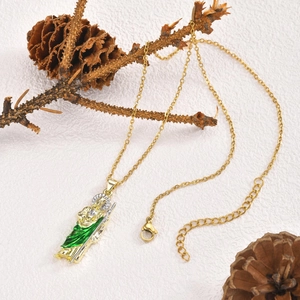 Close-up of gold religious San Judas Tadeo pendant with green enamel on a white surface