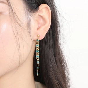 Detail of long gold fringe earrings with turquoise beads on a model's ear