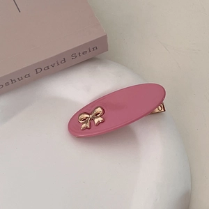 Detail of pink oval hair clip with gold bow accent on aesthetic book background