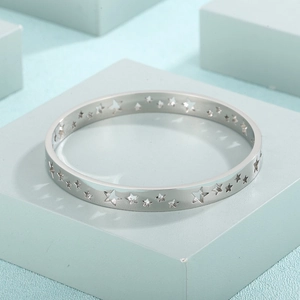 Detailed view of silver stainless steel bangle with hollow star cutouts on blue stand