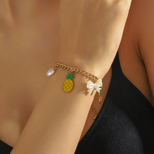 Nahaufnahme eines goldenen Armbands mit Ananas- und Herzanhängern am Handgelenk eines Modells