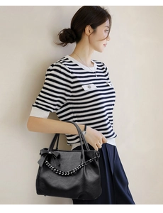 Detail of soft leather black shoulder bag featuring chic bow and thick chain strap