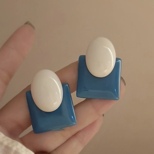 Close-up of retro oval earrings with blue square base and white resin geometric inlay