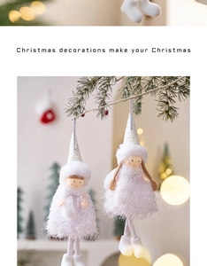 Close-up of white plush Christmas angel dolls hanging on pine branches with warm bokeh