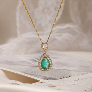 Close-up of teardrop necklace with green gemstone and diamond halo on gold chain