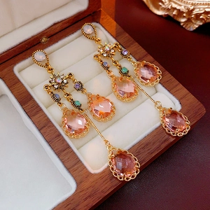 Close-up of gold drop earrings with pink crystal and tassel details in a wooden box